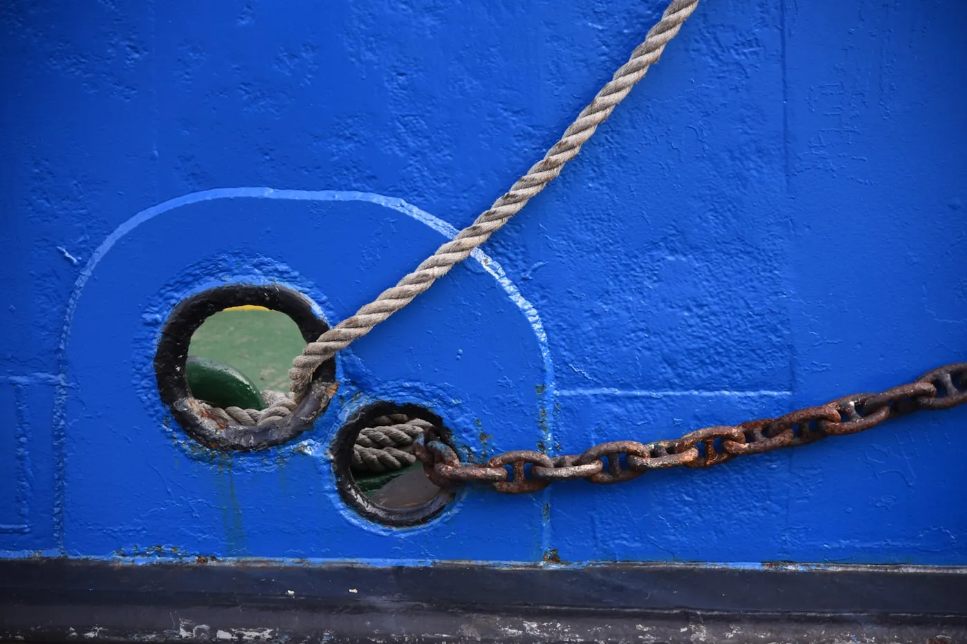 Chaîne rouillée et cordage passés dans les écubiers d’une coque peinte en bleu
