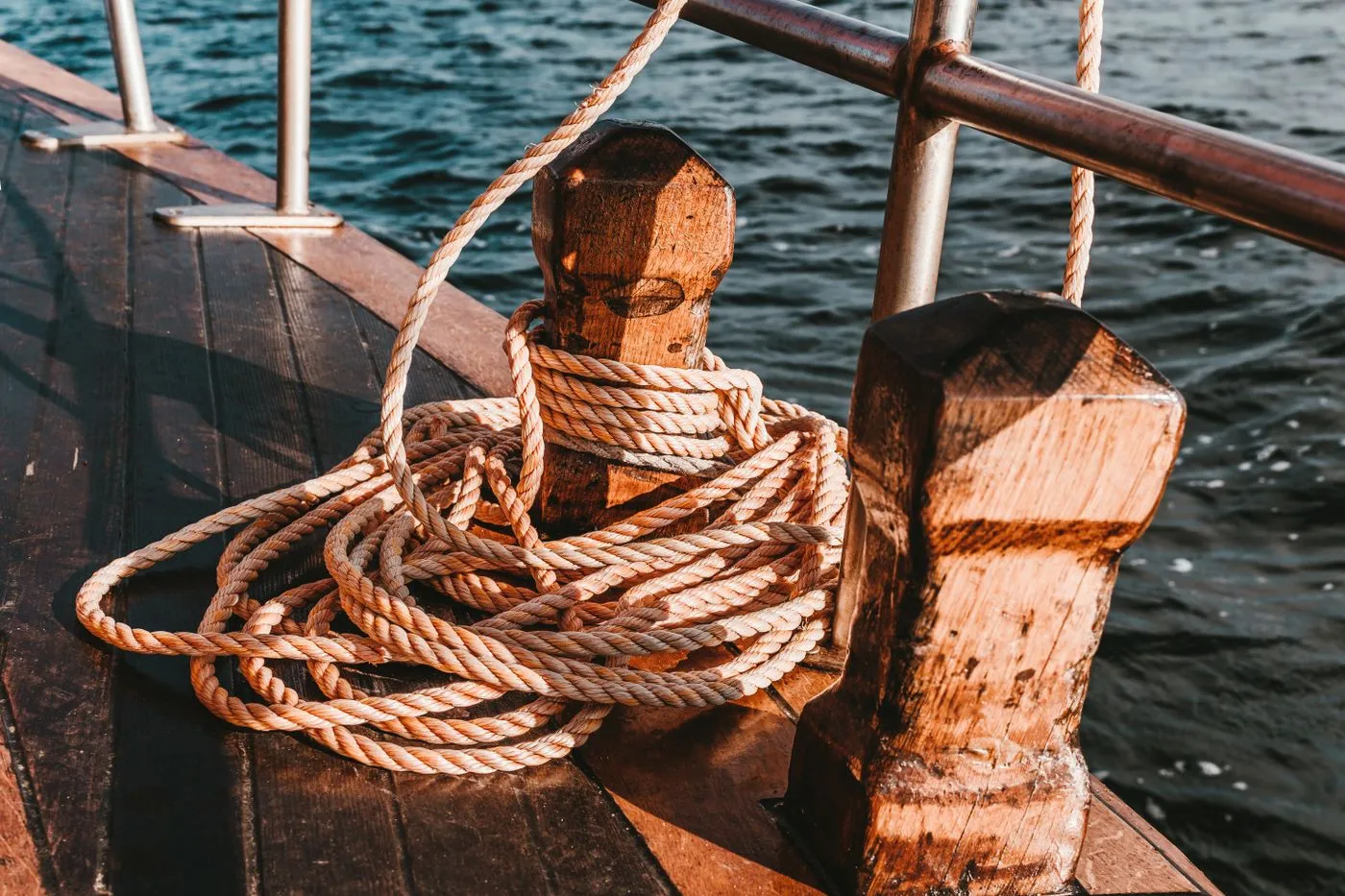 Cordage lové autour d’un taquet en bois sur le pont d’un bateau, l’eau du port derrière