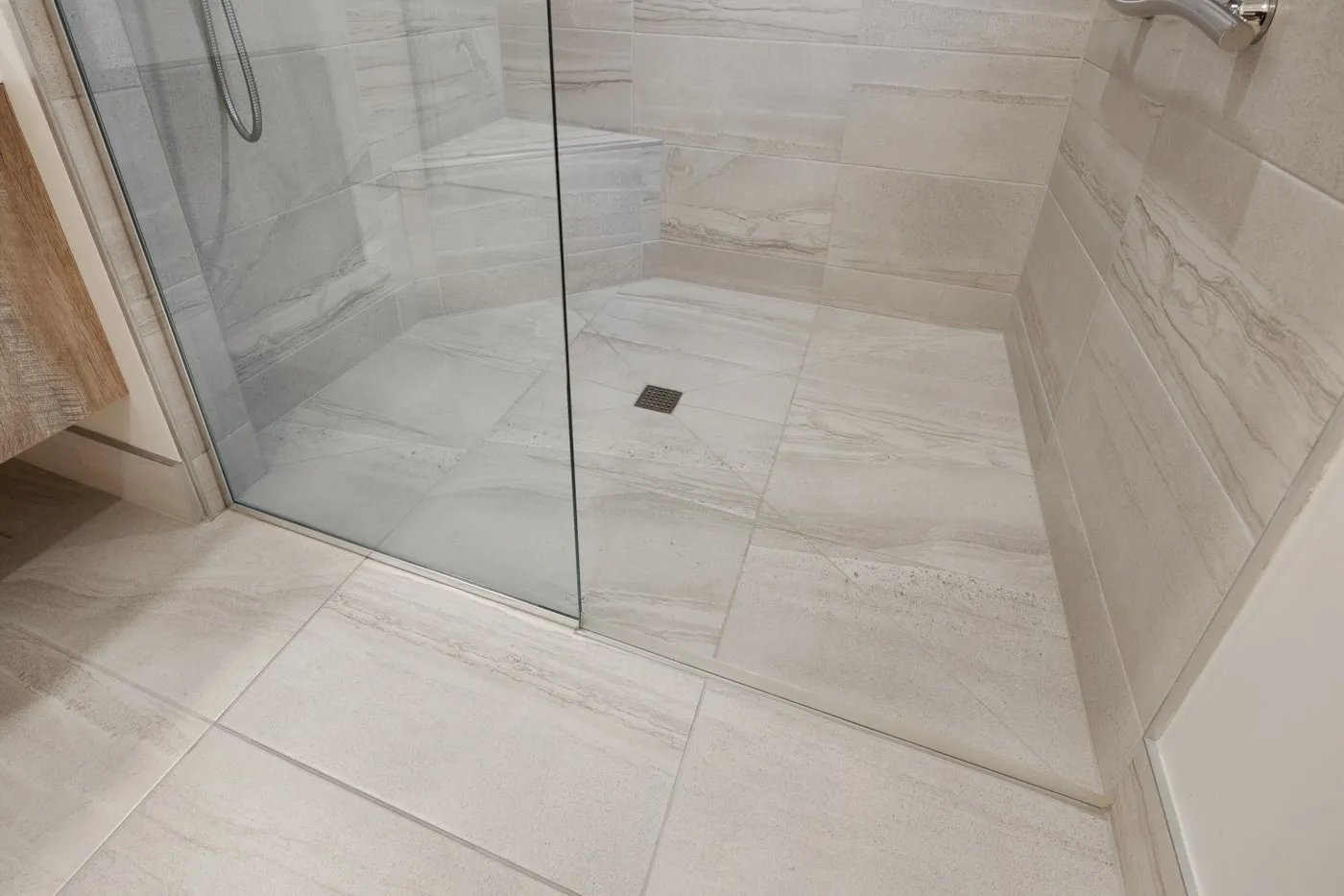 Receveur de douche extra-plat posé au nu d’un carrelage clair, paroi vitrée et bonde centrale