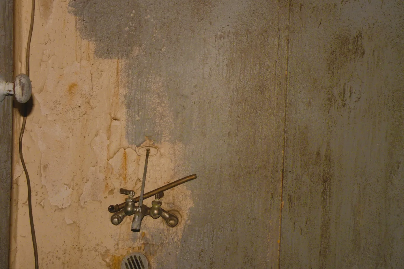 Vieux robinet de puisage en laiton sur un mur enduit taché, siphon de sol au pied