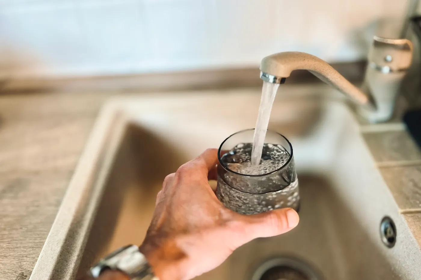 Main tenant un verre sous le mitigeur d’un évier, l’eau tombant en filet